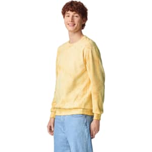A yellow tie-dye crewneck sweatshirt on a model, featuring a relaxed fit and long sleeves. It has a logo.