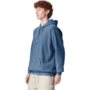 A blue adult hooded sweatshirt with a front pocket and a drawstring hood is displayed on a male model.