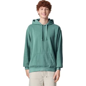 A teal adult hooded sweatshirt featuring a front pocket and drawstring hood, modelled by a smiling person.