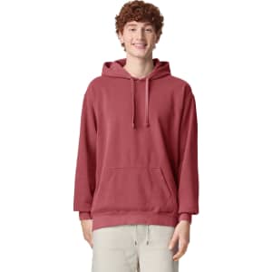 A red adult hooded sweatshirt featuring a front pocket and a logo. The model has a relaxed fit with the hood up.