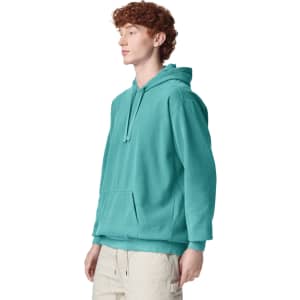 A turquoise adult hooded sweatshirt with a front pocket and a loose fit. The model stands facing to the side.