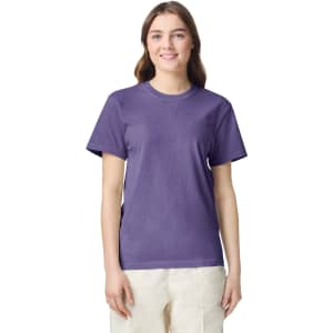 A woman is wearing a purple heavyweight T-shirt. The shirt has a logo and is styled with a relaxed fit.