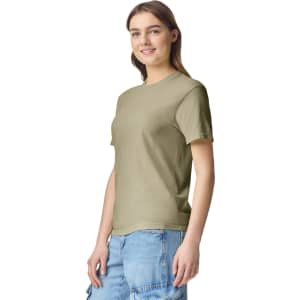 A woman stands wearing an olive green heavyweight T-shirt with short sleeves. The shirt has a logo.