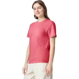 A woman wearing a coral heavy T-shirt, standing with a slight smile, featuring a logo on the shirt.
