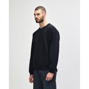 A black crewneck sweatshirt is displayed on a model standing sideways, paired with blue jeans.
