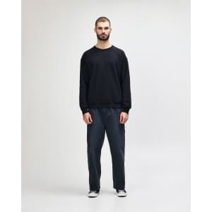 A black crewneck sweatshirt is worn by a person paired with blue jeans and white sneakers, featuring a logo.