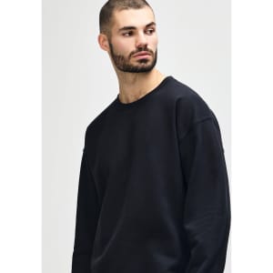 A black Gildan Heavy Blend Adult Crewneck Sweatshirt displayed on a model with long hair, crossing her arms.