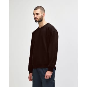 A brown Gildan Heavy Blend adult crewneck sweatshirt worn by a model, paired with blue jeans. The sweatshirt has a simple design.