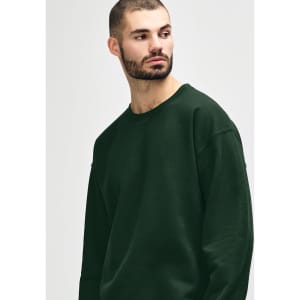 A green crewneck sweatshirt worn by a person, featuring a logo on the sleeve.