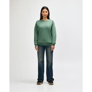 A green Gildan Heavy Blend adult crewneck sweatshirt worn by a model with black jeans and black sneakers. It has a logo.