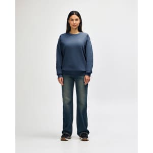 A blue Gildan Heavy Blend crewneck sweatshirt on a model paired with black jeans and sneakers. The sweatshirt has a logo.