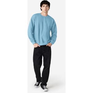 A light blue Gildan Heavy Blend adult crewneck sweatshirt is worn by a model with black jeans and sneakers.