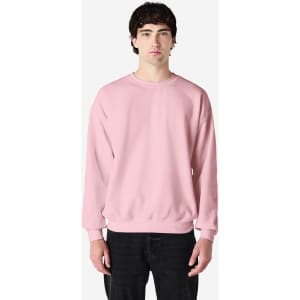 A pink crewneck sweatshirt displayed on a model against a neutral background, featuring long sleeves and a relaxed fit.