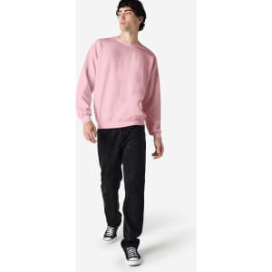 A model wearing a pink Gildan Heavy Blend adult crewneck sweatshirt paired with black jeans and sneakers.
