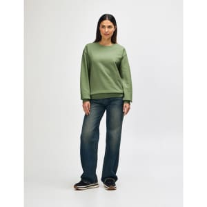 An olive green crewneck sweatshirt worn by a model, paired with black pants and sneakers. It has a logo on the sweatshirt.