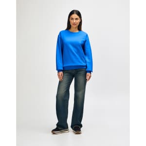 A woman wearing a blue Gildan Heavy Blend crewneck sweatshirt paired with blue jeans and white sneakers.