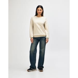 A cream-coloured crewneck sweatshirt is worn by a model paired with light blue jeans and white sneakers.
