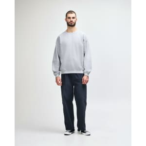 A man wearing a grey crewneck sweatshirt and black jeans, standing in a casual pose against a neutral background.