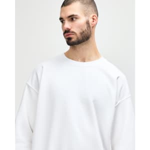 A white Gildan Heavy Blend adult crewneck sweatshirt on a model. The sweatshirt features long sleeves and a relaxed fit.