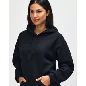 A black Gildan Heavy Blend adult hooded sweatshirt, featuring a drawstring hood and a model adjusting the neckline.