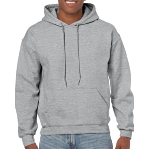 A grey Gildan Heavy Blend adult hooded sweatshirt is displayed on a smiling model, featuring a front pocket and drawstrings.