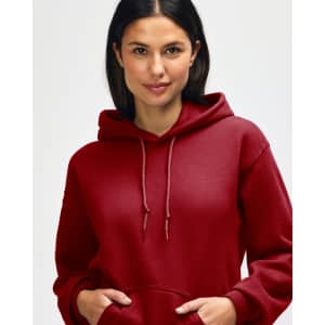 A red hooded sweatshirt is worn by a young man adjusting the hood near his face. The sweatshirt features a logo.