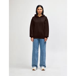 A brown hooded sweatshirt with a front pocket, worn by a model paired with dark jeans and sneakers.