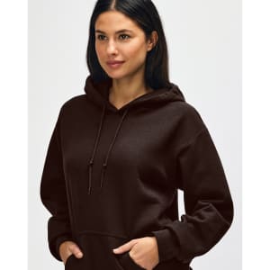 A brown hooded sweatshirt featuring a drawstring hood and a model adjusting it. The design has a logo.