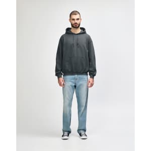 A grey Gildan Heavy Blend adult hooded sweatshirt worn by a model, paired with blue jeans and white shoes.