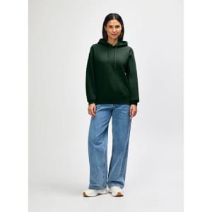 A woman wearing a green hooded sweatshirt with a kangaroo pocket, paired with blue jeans and white sneakers.