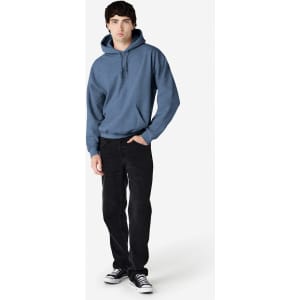 A man wearing a blue hooded sweatshirt and black trousers, standing against a plain background. The sweatshirt has a logo.