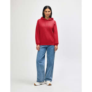 A red hooded sweatshirt worn by a model with jeans and sneakers, featuring a front pocket and drawstring hood.