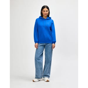 A blue hooded sweatshirt paired with jeans, featuring a front pocket and drawstring hood, modelled by a woman.