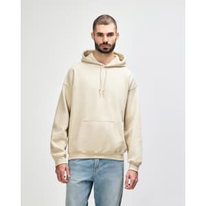 A beige hooded sweatshirt with a front pocket and drawstrings, worn by a model. It features a logo.