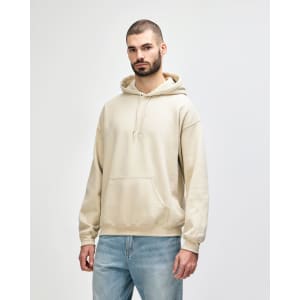 A light beige hooded sweatshirt with a front pocket and drawstrings, worn by a model. The garment has a logo.