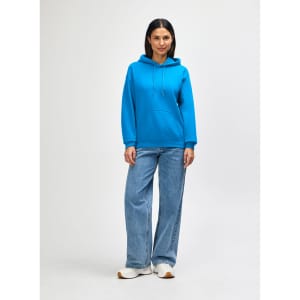 A woman in a bright blue hooded sweatshirt and jeans stands with her hands in the pockets.