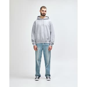 A grey hooded sweatshirt is worn by a male model, paired with black jeans and sneakers. The sweatshirt has a logo.
