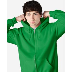 A green full zip hooded sweatshirt with a hood, worn by a model adjusting it. The sweatshirt features a logo.