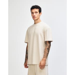 A unisex mockneck t-shirt in a neutral beige colour, displayed from the side, featuring a simple design and logo.