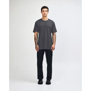 A unisex fine jersey short sleeve t-shirt in black, worn with beige pants and blue sneakers, with a logo visible.