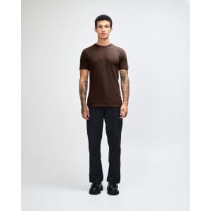A unisex fine jersey short sleeve T-shirt in olive green, worn with light blue jeans. The model stands casually with hands in pockets.