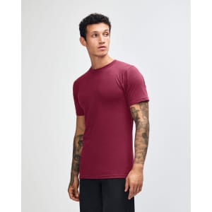 A unisex fine jersey short sleeve t-shirt in burgundy, featuring a logo, displayed on a male model from the side.
