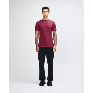 A maroon unisex short sleeve t-shirt is worn with khaki cargo pants. The model has long hair and a casual pose.