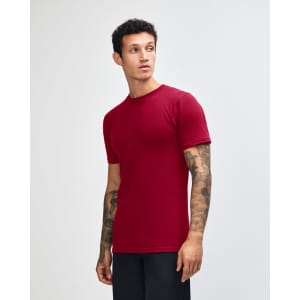 A maroon unisex short sleeve t-shirt displayed on a model from the side, featuring a plain design and a logo.