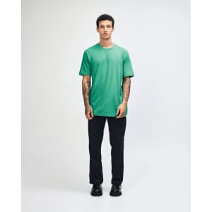A model wearing a turquoise unisex fine jersey short sleeve t-shirt paired with khaki pants. The shirt has a logo.