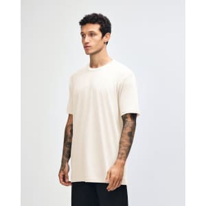 A side view of a beige unisex short sleeve t-shirt worn by a model, featuring a logo on the sleeve.