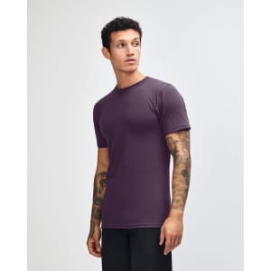 A purple unisex short sleeve t-shirt displayed from the side, featuring a simple design and a brand logo.
