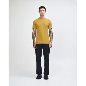 A model wearing a mustard yellow unisex short sleeve t-shirt paired with light blue baggy jeans and black shoes.