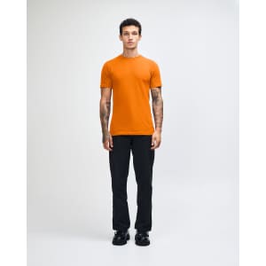 An orange unisex short sleeve t-shirt worn by a model, paired with beige cargo pants. The t-shirt features a logo.