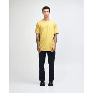 A model wearing a yellow unisex fine jersey short sleeve t-shirt and loose blue denim jeans, hands in pockets.